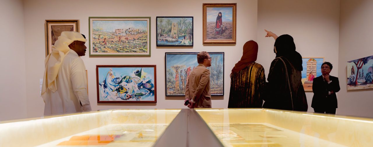 Visitors viewing framed modern Saudi paintings in a gallery room