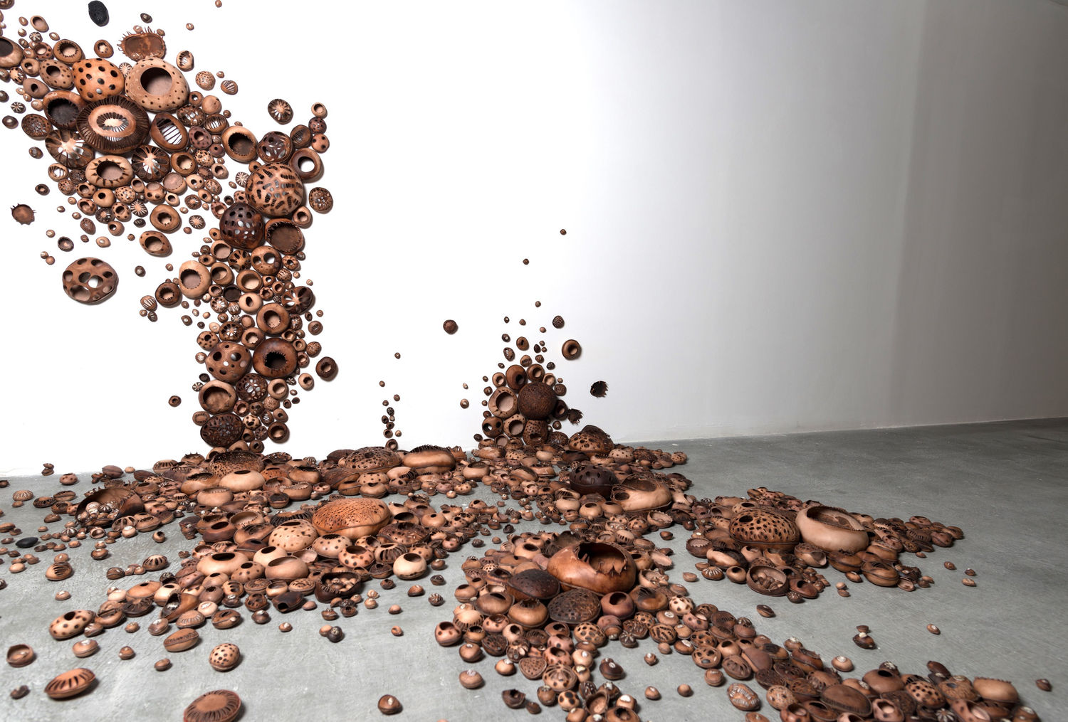 Hundreds of small clay vessels spilling from a gallery wall onto the floor