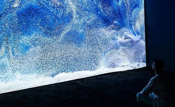 A visitor seated before a vast blue digital ocean projection