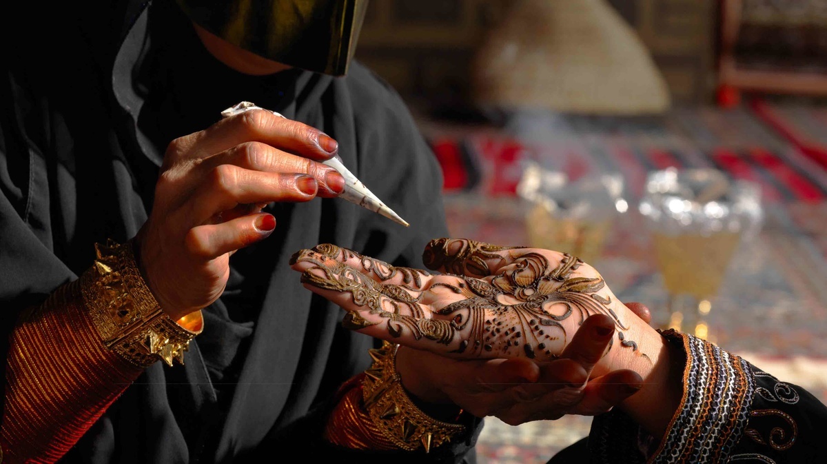 A henna artist applying intricate patterns on a guest's hand in warm desert light